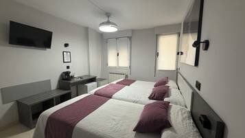 A hotel room with two beds, a desk, a chair, a TV, and a window.