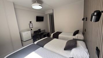 Habitación de hotel con dos camas, un escritorio, una silla, un televisor, una cafetera y un refrigerador.