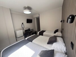 Habitación de hotel con dos camas, un escritorio, una silla, un televisor, una cafetera y un refrigerador.