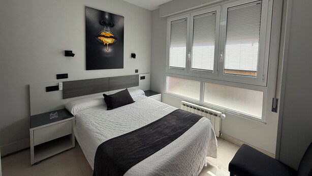 Ein modernes Schlafzimmer mit einem großen Bett, einem Nachttisch, einer Wandleuchte und einem Fenster mit Jalousien.