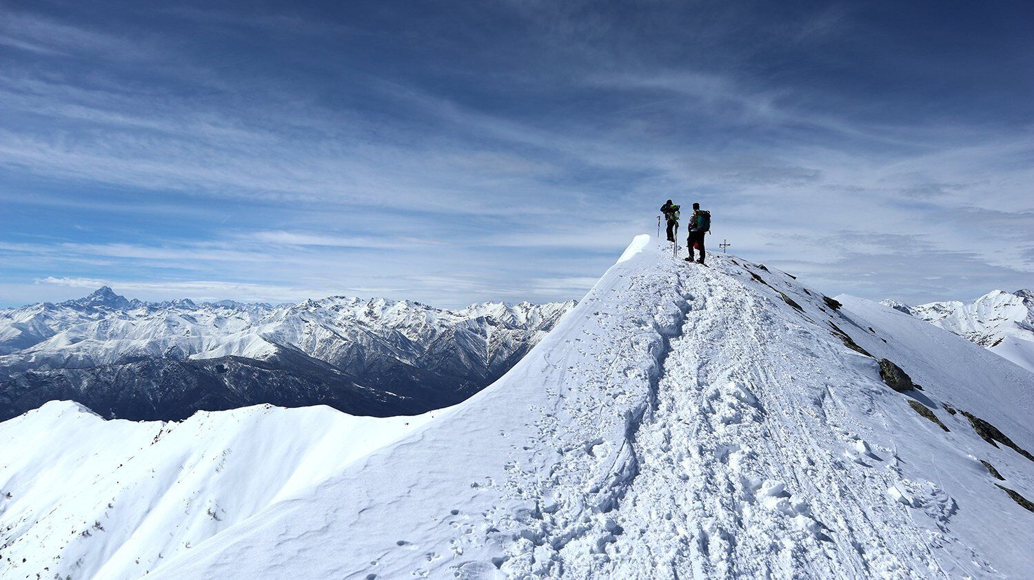 A snowy mountain peak with two hikers at the summit.
