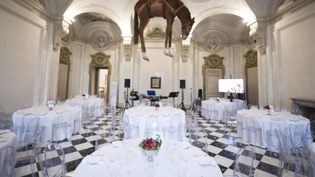A banquet hall with round tables, clear chairs, and a checkered floor. - VILLA FIORITA LAKE VIEW APARTMENT (Avigliana)