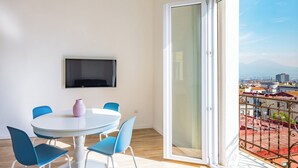 A room with a round table, blue chairs, a pink vase, and a TV on the wall. - Sunny Panoramic Apartment by Napoliapartments (Naples)