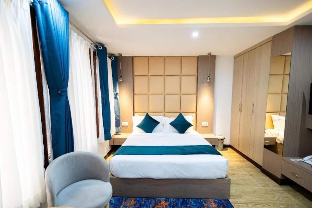 A hotel room with a large bed, a chair, a desk, and a wardrobe.