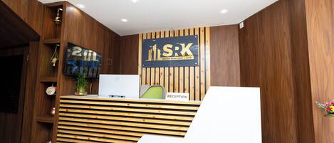 A reception desk with a wooden finish, a sign reading "S.R.K Service Apartment & Hotel," and a reception area with a white counter.