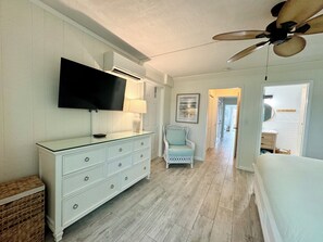 Ein Schlafzimmer mit Deckenventilator, Fernseher, Kommode, Stuhl und Bett.