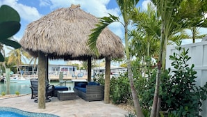 Un espace piscine agrémenté d’un gazebo à toit de chaume, de chaises longues et d’une petite piscine.