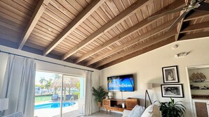 Un salon doté d’un grand téléviseur, d’un canapé, d’une table basse et offrant une vue sur une piscine et un espace extérieur.