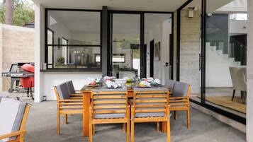 A modern outdoor dining area with a glass-enclosed patio, a barbecue grill, and a view of the interior.