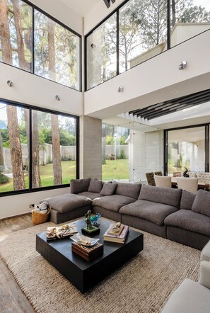 Ein modernes Wohnzimmer mit Ecksofa, Couchtisch und großen Fenstern mit Blick auf Bäume und einen Garten.