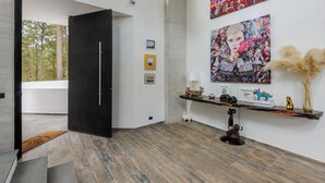 A modern interior with a black door, a wooden floor, a console table with decorative items, and two large framed artworks on the wall. - Casa María (Valle de Bravo)