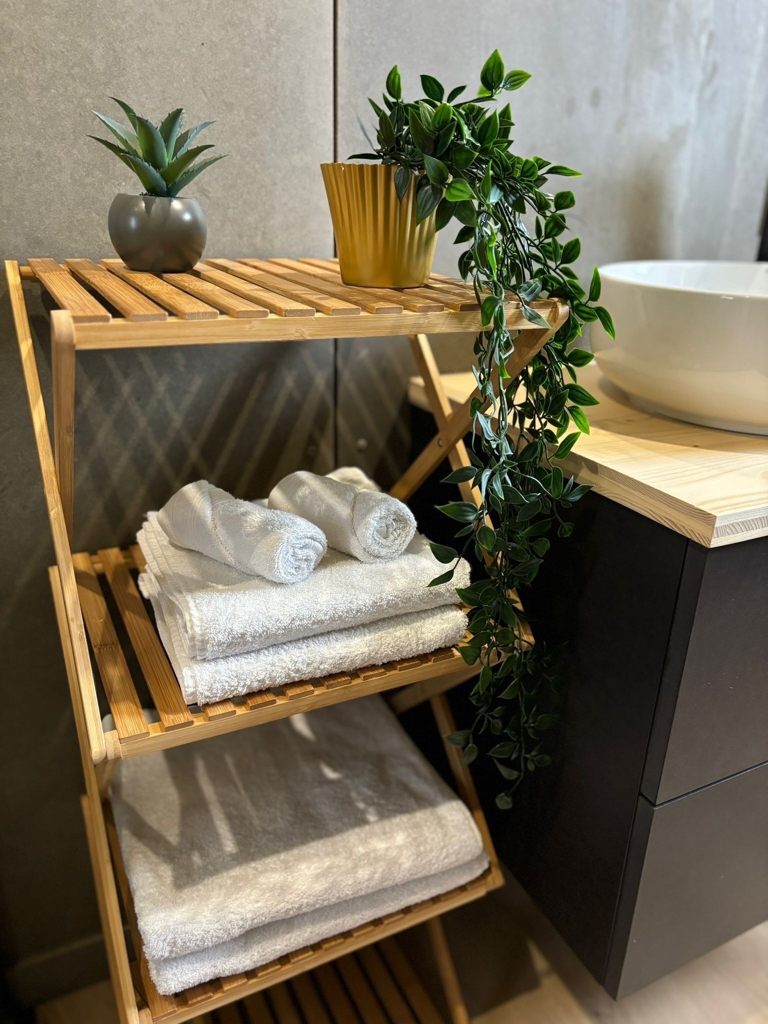 A wooden shelf with folded towels and a potted plant.