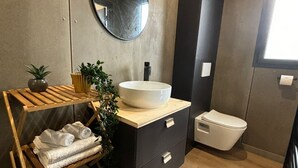 Een moderne badkamer met een houten wastafelmeubel, een ronde spiegel, een witte wasbak en een toilet.