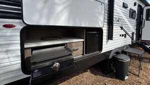 A travel trailer with a kitchen area, including a stove, a sink, and a trash can.