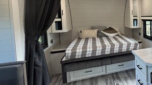A compact RV bedroom with a bed, built-in cabinets, and a window.