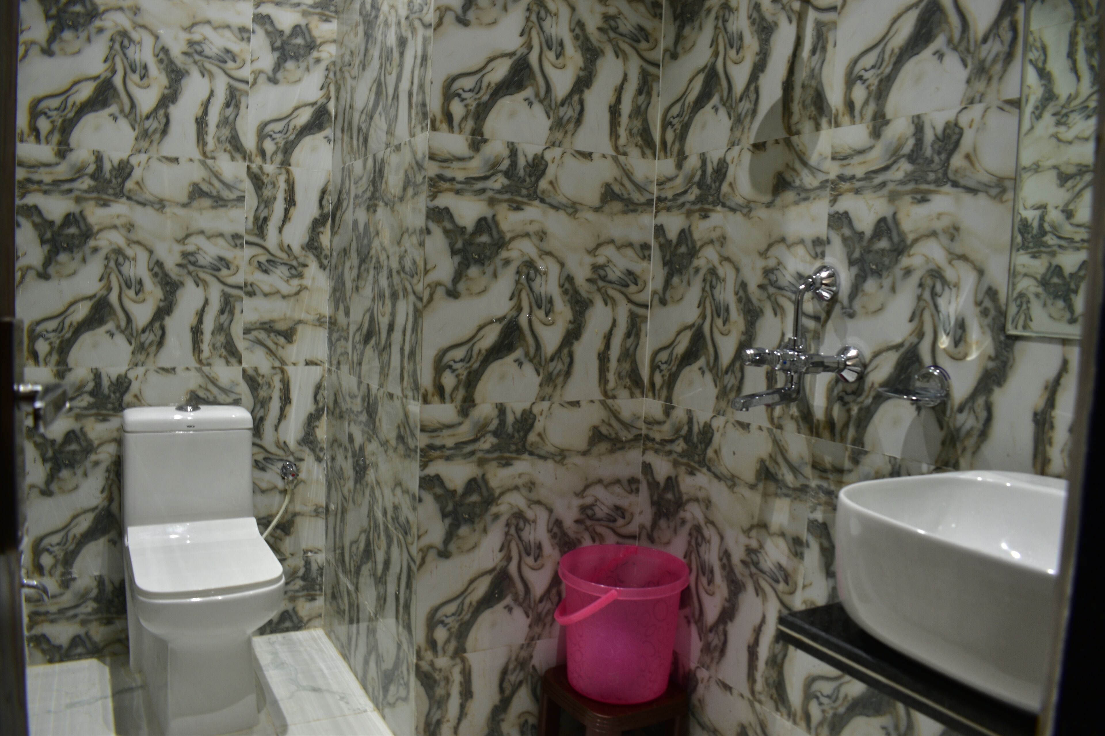 A bathroom with a toilet, sink, and marble-patterned walls.