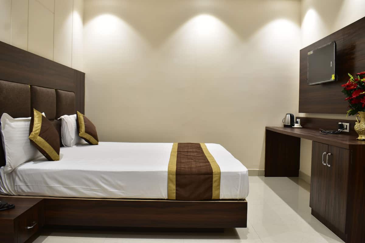 Hotellihuone, jossa on suuri sänky, puinen pääty, seinälle asennettu taulutelevisio ja pieni työpöytä, jossa on kahvinkeitin.