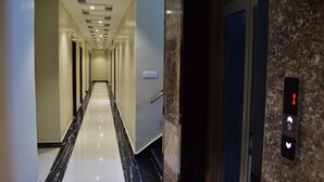 A modern hotel corridor with a marble floor, a wall-mounted elevator, and a ceiling with recessed lighting. - HOTEL KUSUM PALACE (Gaya)