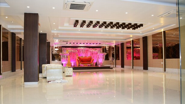 A spacious lobby with a polished floor, a central stage with a red chair, and a floral backdrop. - HOTEL KUSUM PALACE (Gaya)