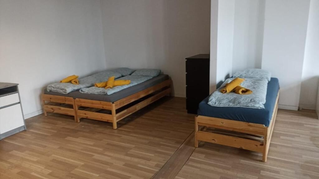 Una habitación con dos camas de madera, una más grande y otra más pequeña, ambas con ropa de cama azul y almohadas amarillas.