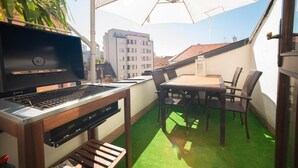 En balkon med grill, spisebord, stole og parasol.