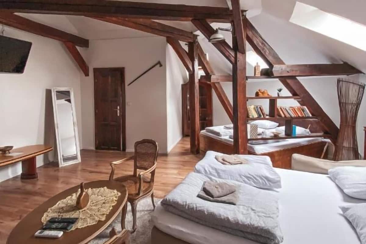 Une chambre confortable située sous les toits, avec des poutres apparentes, un lit en mezzanine, un petit bureau et une chaise.