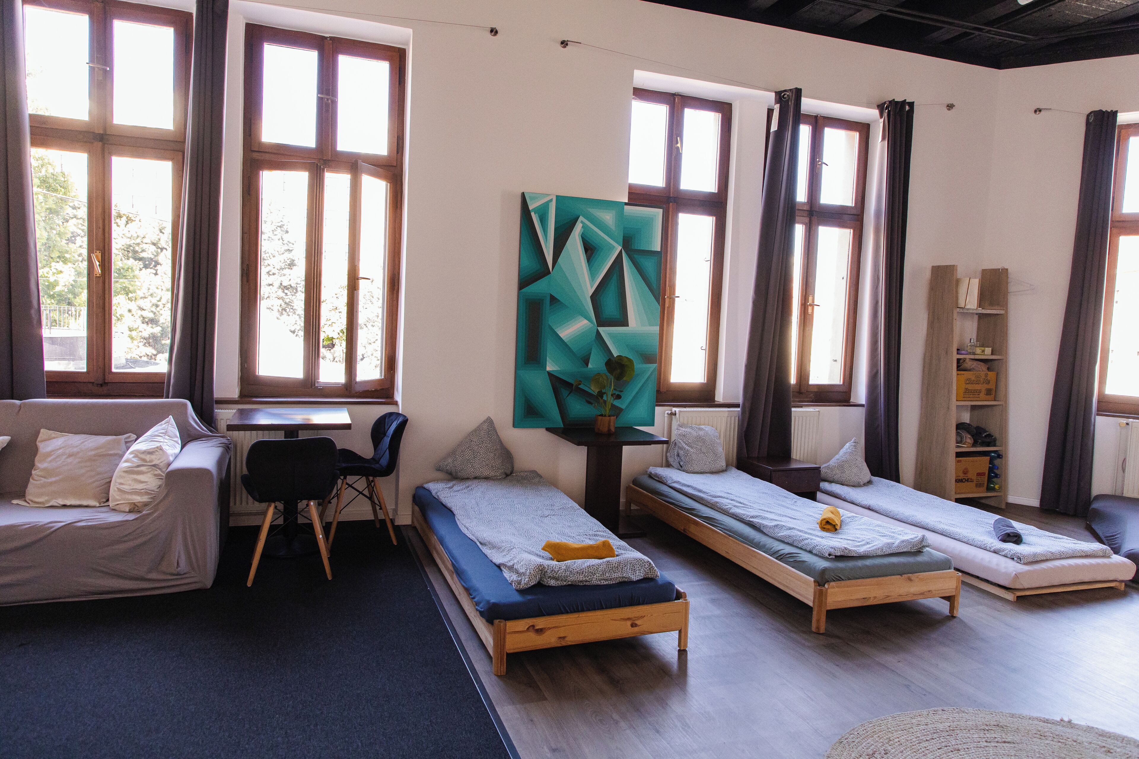 Una habitación moderna y bien iluminada con dos camas individuales, un sofá, un escritorio y un cuadro abstracto grande.