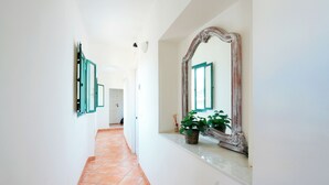 A hallway with a tiled floor, a large mirror with a rustic frame, and a potted plant on a shelf. - Currò Palace (Catania)