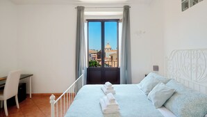 A bedroom with a bed, a desk, and a view of buildings through a window. - Currò Palace (Catania)