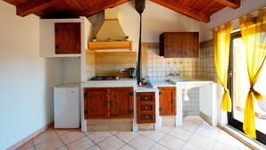A kitchen with wooden cabinets, a white refrigerator, a gas stove, and a window with yellow curtains. - Currò Palace (Catania)