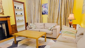 A living room with a sofa, a coffee table, a lamp, a fireplace, and a bookshelf. - Gardner's Crescent City Apartment (Edinburgh)