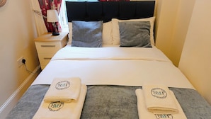 A neatly made bed with a white duvet, grey and white pillows, and two towels with a logo on them. - Gardner's Crescent City Apartment (Edinburgh)