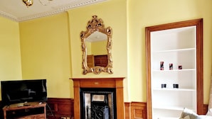 A living room with a fireplace, a television, and a bookshelf. - Gardner's Crescent City Apartment (Edinburgh)