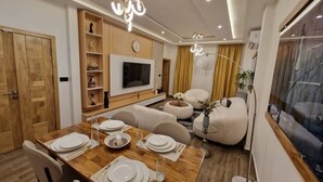 Una sala moderna con una mesa de comedor de madera dispuesta para cuatro personas, un sofá y un televisor montado en la pared.