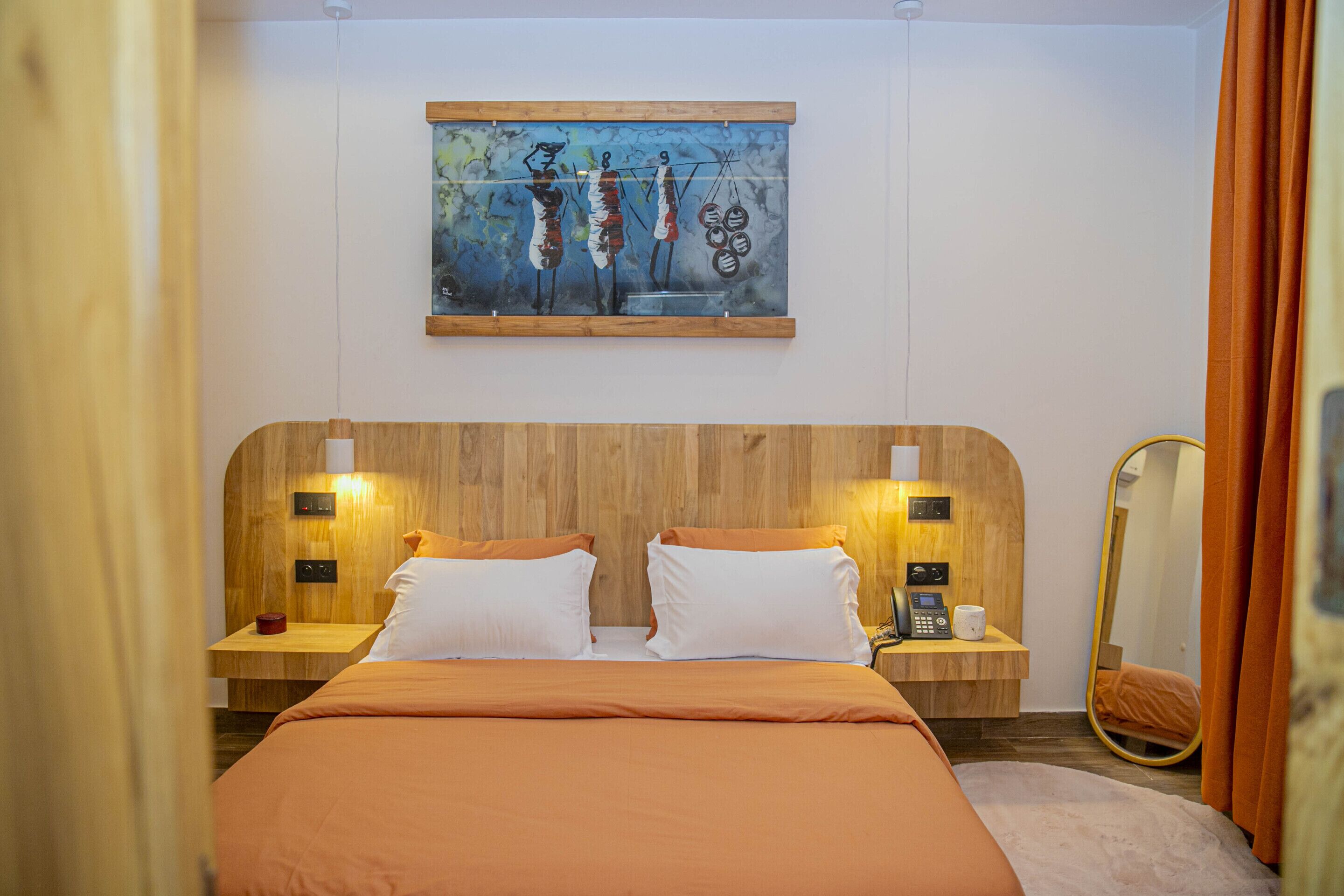 A hotel room with a wooden headboard, two bedside tables with lamps, a painting on the wall, and a mirror on the wall.