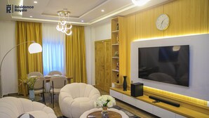 Una sala de estar moderna con un televisor de pantalla plana, asientos cómodos, un comedor y una estantería de madera.