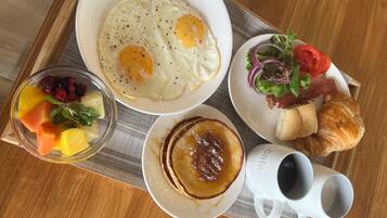 Bandeja de café da manhã com ovos, frutas, panquecas, croissant, salada e café.