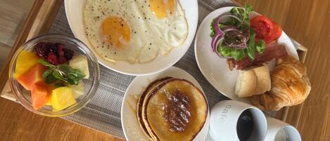 A breakfast tray with eggs, fruit, pancakes, croissant, salad, and coffee.