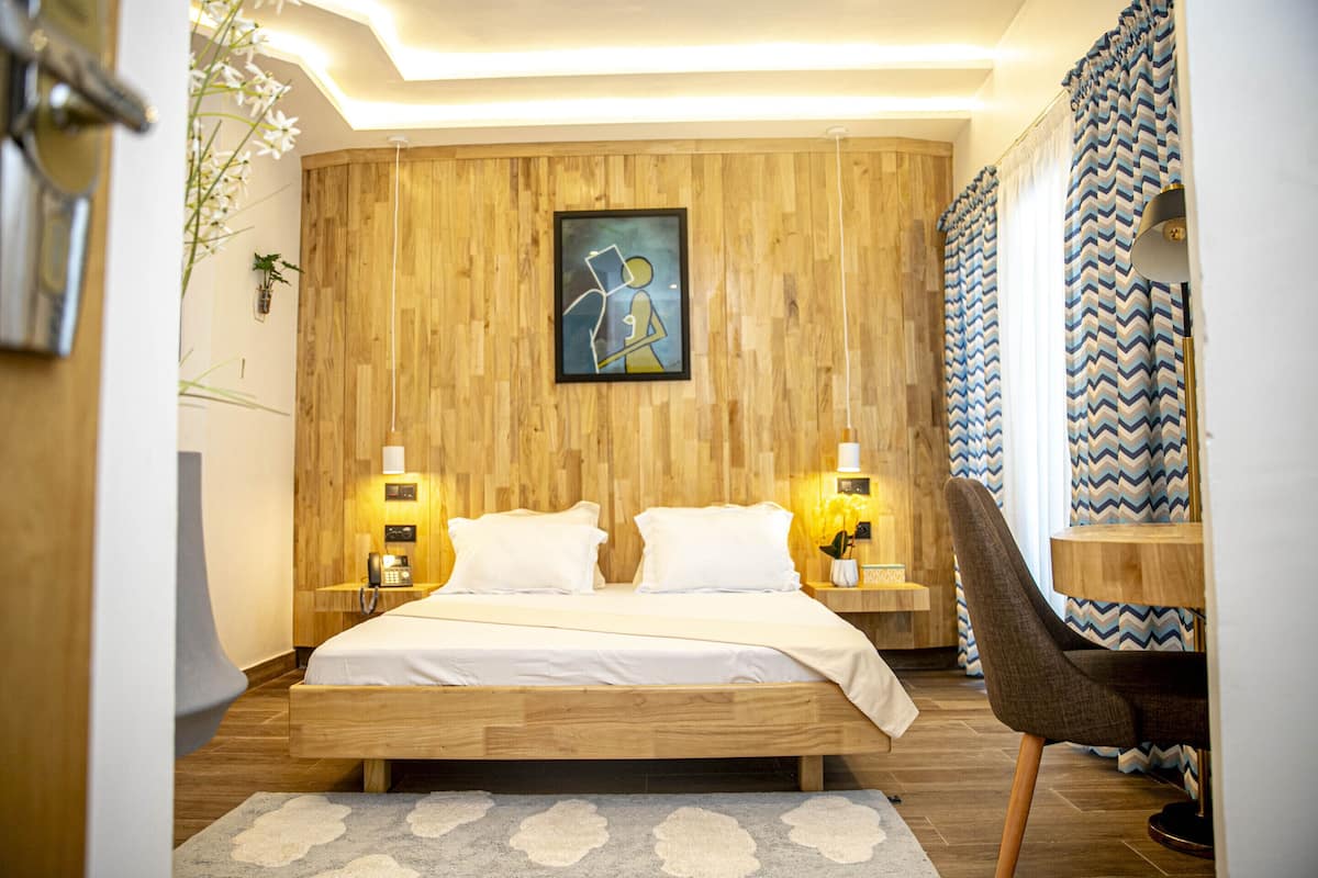Una camera da letto con una testiera in legno, un letto con lenzuola bianche, due lampade da comodino, un quadro appeso al muro e un tappeto decorato.