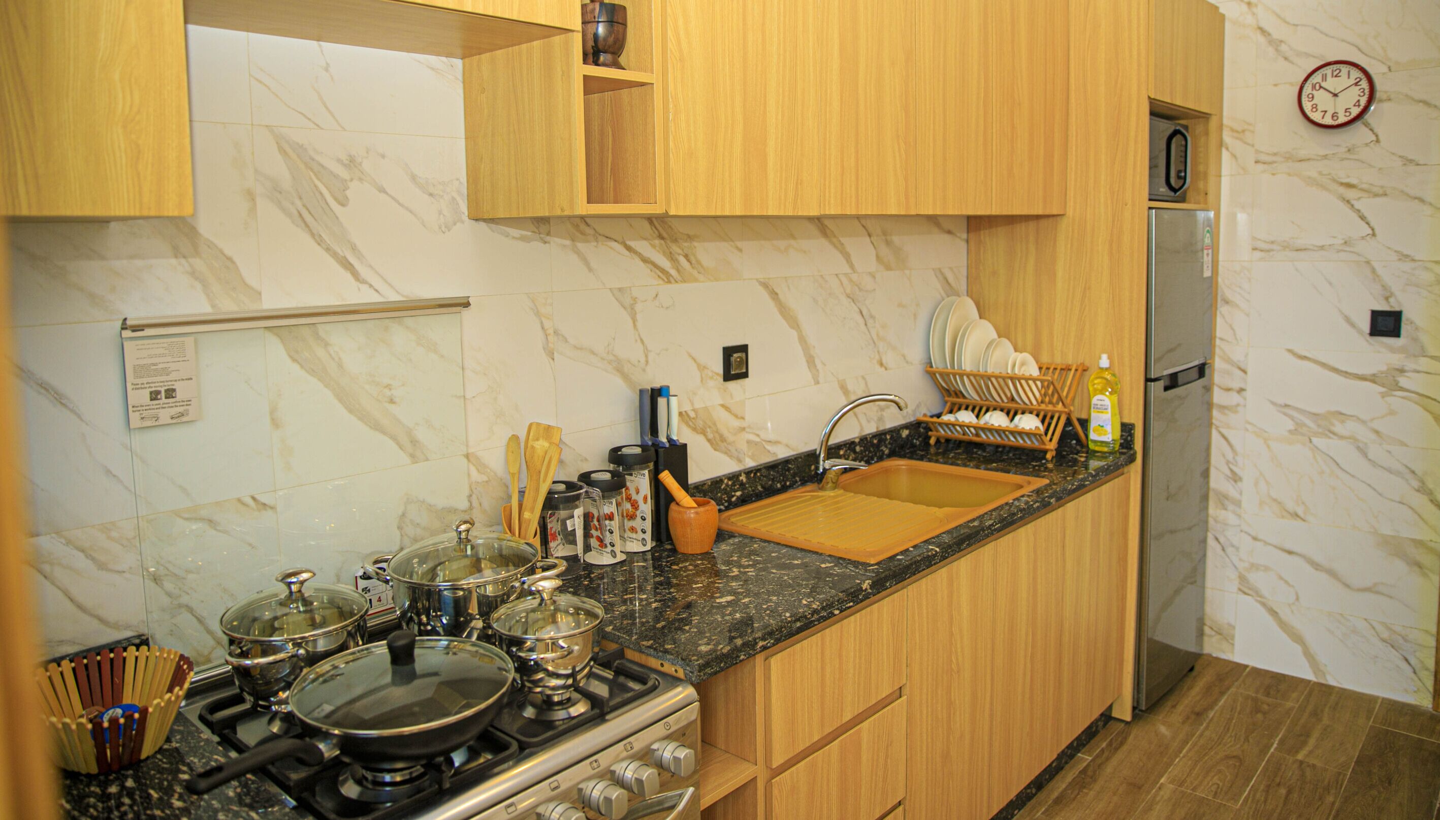 Una cocina con estufa, fregadero, armarios de madera, salpicadero de mármol y un reloj en la pared.