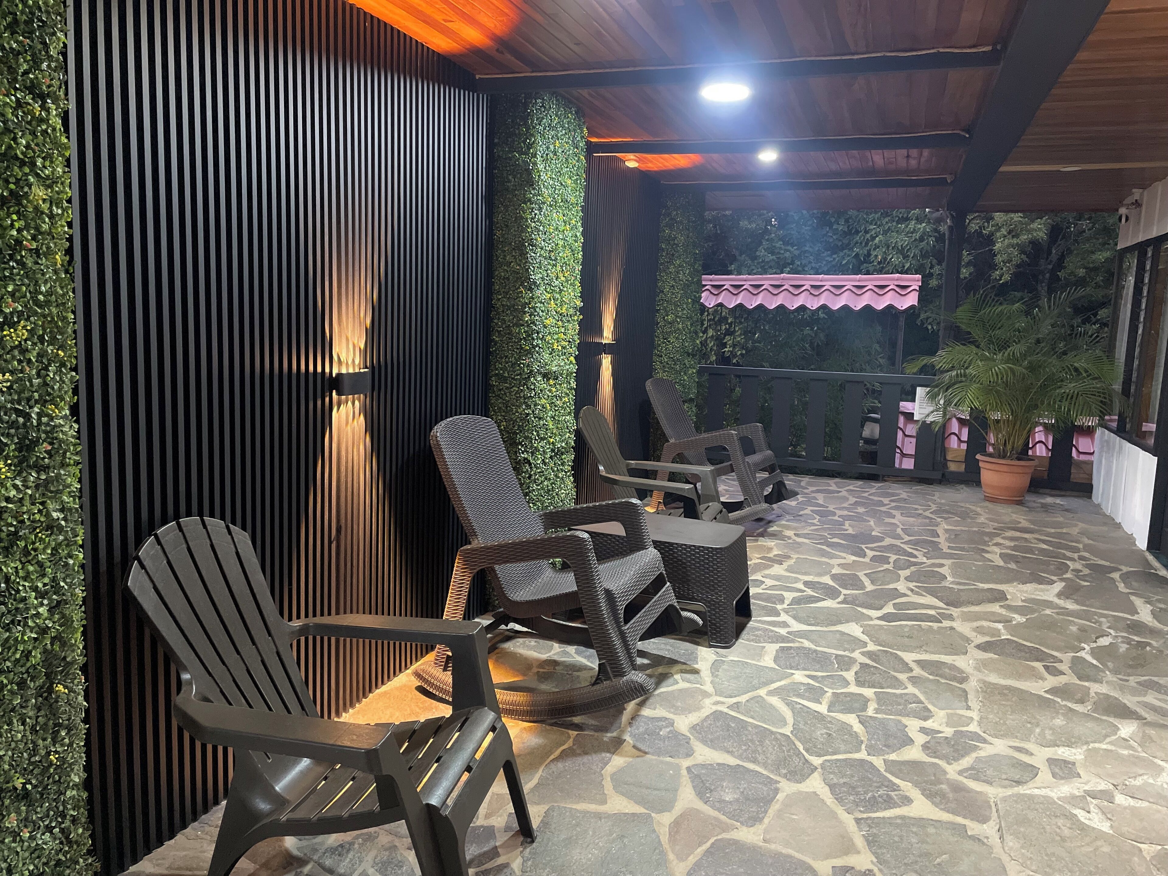 A covered outdoor seating area with stone flooring and wicker furniture.