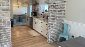 Une cuisine avec des murs en briques apparentes, un plancher en bois et un lave-vaisselle encastré.