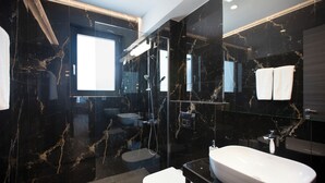Une salle de bain moderne avec une grande baignoire blanche, une douche à parois de verre et un pare-baignoire en marbre foncé.