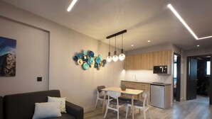 Un salon moderne avec un canapé foncé, une table à manger avec des chaises, un coin cuisine doté de meubles en bois et un luminaire suspendu.