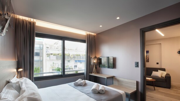 Une chambre d’hôtel moderne, dotée d’un grand lit, d’un bureau, d’une chaise, d’une télévision et offrant une vue sur la ville par la fenêtre.