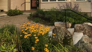 A two-story house with a star-shaped decoration on the facade, a front porch, and a garden with yellow flowers.