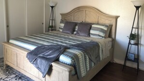 Ein Schlafzimmer mit Bett, Nachttisch, Wandlampe und einem gerahmten Zitat an der Wand.