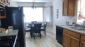 Eine Küche mit Essbereich, Granit-Arbeitsplatten, Holzschränken, einem schwarzen Kühlschrank, einem Herd, einem Geschirrspüler und einem Fenster mit Jalousien.