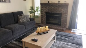 Ein Wohnzimmer mit einem dunkelgrauen Sofa, einem Holztisch mit Kerzen, einem Kamin und einem Stadtbild an der Wand.