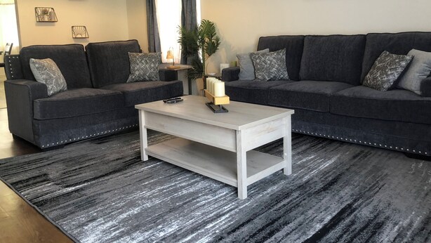Ein modernes Wohnzimmer mit zwei dunkelgrauen Sofas, einem weißen Couchtisch und einem gemusterten Teppich.